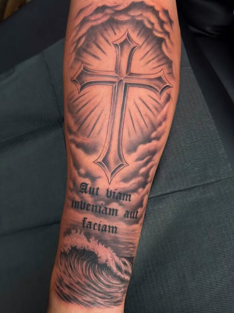 Cross with rays and latin script forearm tattoo